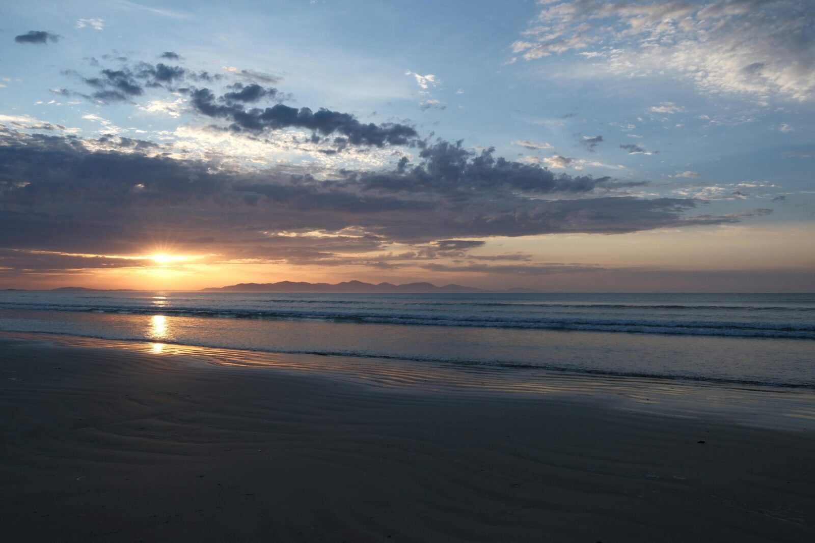 A serene sunset over the ocean with gentle waves and a peaceful sky.